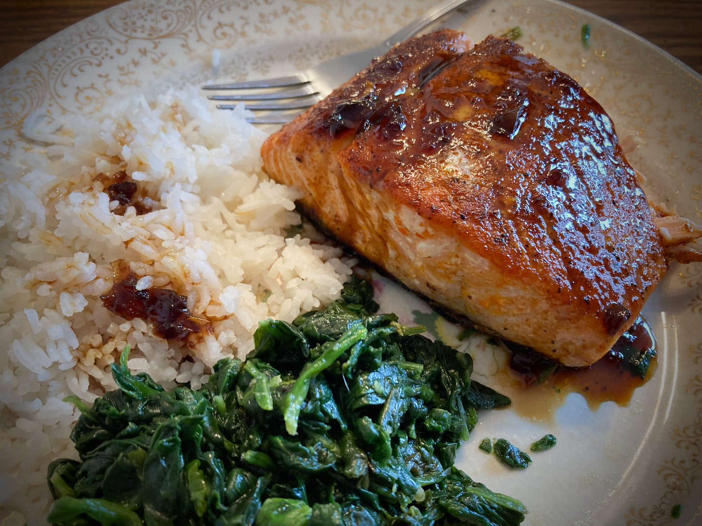 Plated dish with salmon, rice, and greens on a decorative plate.