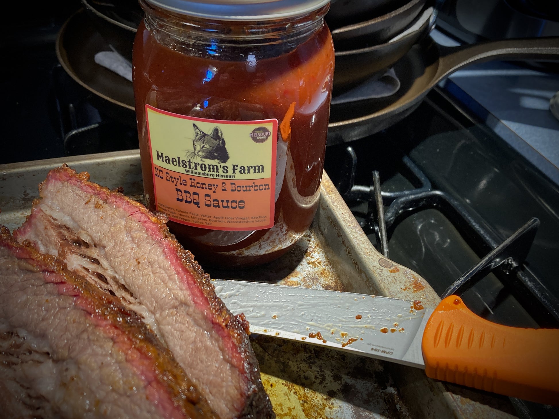 Jar of Haelstrom's Farm BBQ Sauce on a grill with sliced meat and a knife.